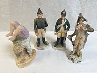 Four vintage porcelain figurines arranged including military and a whimsical child doing a handstand showing overall condition and detail.