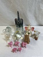 Full view of the 11 assorted elephant figurines in clear glass, pink glass, ceramic, crystal, and carved materials.