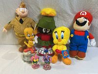 Arrangement of all plush toys and figurines showing Garfield, Marvin the Martian, Mario plush, both Tweety Bird plush dolls, Pink Panther figurines, Tweety Bird figurine in glass dome, and two flamingo figurines.