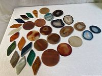 Photo showing all 20 polished agate slices and shapes laid on white surface, highlighting round, oval, diamond, and other geometric cuts in assorted natural and dyed colors