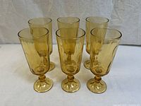 Front angle view of six amber glass goblets arranged in two rows of three, showing the taller silhouette and rounded footed bases.