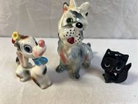 Front view of three vintage anthropomorphic ceramic animal figurines: two dogs and one black cat, positioned on a gray surface with a plain background.