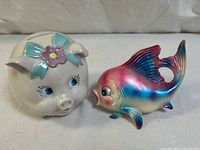 Two-piece ceramic figurine set showing vintage piggy bank and iridescent fish