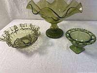 Front view of all three green glass compote dishes showing various ruffled edges and pedestal bases.