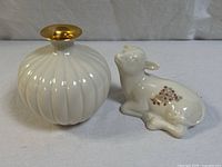 Photo showing white ribbed ceramic vase with gold rim and ceramic lamb figurine side by side on neutral background