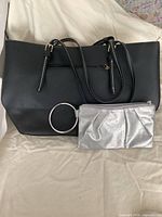 Black tote bag with matching black wallet and silver evening clutch bag laid flat showing front and strap details.