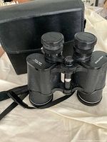 Photo showing Pentex binoculars with black carrying case on fabric surface.
