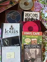 Lot of 9 music CDs including Louis Armstrong, Vinyl Cafe, Radio Days, and Beautiful Blends, shown with cover art and discs visible.