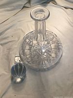 Crystal wine decanter with a wide patterned base and slim neck, shown next to the detached round stopper with vertical ribbing.