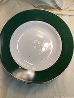 Close-up of a single green and gold rimmed bowl showing white interior and shiny ceramic finish