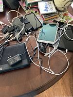 Top-down photo showing four phones, three tablets, several chargers and cords, and a Bell router/modem on a wooden table.