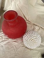 Overview of orange frosted glass vase and white shell sphere together on beige fabric.