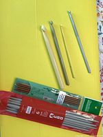 Photo showing four crochet hooks and two sets of packaged knitting needles.