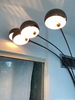 Photo showing four globe-shaped light fixtures lit on black curved arms extending overhead with shadows cast on the wall.