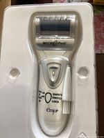 Emjoi Micro Pedi electronic foot file in plastic packaging showing safety lock switch and roller head