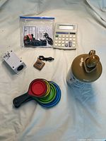 Entire lot arranged on fabric background showing measuring cups, calculator, whiskey crock, plug adapter, keychain, light timer, flashlight, and charging cable in plastic bag