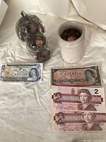 Containers holding Canadian pennies along with multiple Canadian paper currency bills, including a 1 dollar bill and several 2 dollar bills.