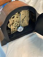 Rear view of the clock showing mechanical movement, brass gears, pendulum, and winding mechanism.