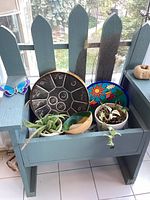 Front view of wooden blue planter bench with potted plants and decorative plates inside the planter section.