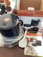 Side angle photo of the black Wolfgang Puck personal rice cooker next to its original box showing branding and product image.