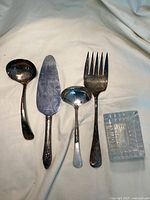 Photo showing two ladles, serving fork, pie server, and small glass dish on beige fabric background