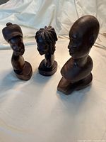 Three wood bust carvings including two men and one woman with detailed hair and hats.