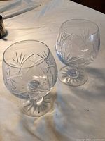 Two clear glass brandy snifters with geometric cut patterns seen from above on beige fabric background.