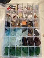 Top view of compartmentalized container with sections holding sorted sea glass, shells, and stones in various colors and shapes.