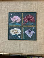 Full view of the framed tile with four painted flowers separated by bamboo-like gold lines.