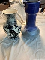 Front view of two vases, one gray sculptured with artwork and one tall blue glazed vase