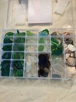 Plastic organizer box compartments filled with assorted sea glass sorted by color - green, white, brown, and clear glass pieces.