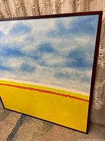 Front angle showing blue and white clouds in upper sky and yellow field below with red and white stripes, mounted in a solid dark wood frame.