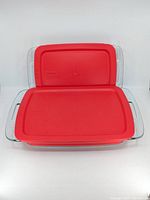 Two Pyrex rectangular glass baking dishes stacked with red plastic lids on top in a front-facing view.
