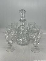 Full set of 6 crystal glasses and 1 decanter with stopper arranged together, showing pinwheel design and clear crystal material.