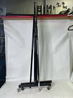Folded clothing rack showing the base with caster wheels and vertical poles in black and silver finish.