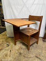 Side view of antique wooden schoolhouse desk showing attached chair and storage shelf underneath.