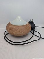 Aroma diffuser with wood grain finish and white diffuser top placed on a surface, cord attached, showing overall front and side design.