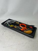 Black plastic rectangular tray filled with assorted hand tools including a stapler, wire strippers, pliers, measuring tape, wrench, and chalk line.