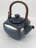 Blue Japanese teapot with rectangular body, wicker handle, and lid seen from an oblique front angle