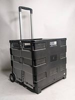 Side view of the black foldable rolling cart with extended telescoping handle and wheels.