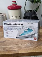 Sealed box of Hamilton Beach Steam Iron on wooden surface.