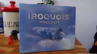 Front cover of the sealed photo album titled 'Iroquois Rollout,' showing a close-up image of an aircraft engine against a sky background.