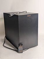 Front and side view of black Klipsch wireless subwoofer with power cord and remote placed in front.