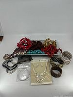 Overview of mixed jewelry including necklaces, bracelets, earrings, and accessories arranged with visible mirrored dish and packaged necklace set