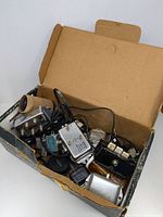 Box of assorted AV components including coaxial splitters, amplifiers, and cable connectors in a worn cardboard box.