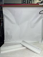 Two white IKEA Mosslanda wall shelves leaning against a white backdrop on the floor, showing both shelf sizes and groove detail.