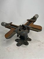 Full view of the picture frame vise showing two clamping arms, the swivel base with mounting holes, and adjustment screws with knurled metal handles.