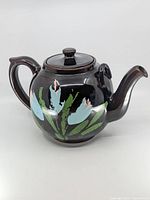 Front and side view of the black ceramic tea pot showing floral patterns in blue, light pink, and green with a glossy finish.