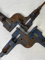 Close-up of two blue cast iron corner clamps with rust, showing the corner angle and threaded tightening screws.