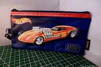 Front view of vintage Hot Wheels pencil case showing vibrant car graphic and Hot Wheels logo with red zipper on dark blue fabric.